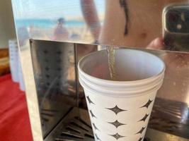 Water is poured into a disposable paper cup for drinking from a cooler with water and drinks, close-up view. Faucet for pouring drinks photo