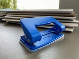 Blue iron metal office punch for punching holes in sheets of paper and documents on the working business table in the office. Stationery photo