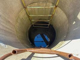 A large round deep well made of concrete rings with clean well underground water for drinking with old rusty stairs