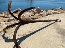 la parte final de un viejo ancla de hierro oxidado, colocada sobre un fondo de piedra como recuerdo para los turistas foto