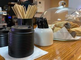 palos desechables de madera natural para mezclar azúcar en té o café, azucarero, tapas térmicas de plástico para tazas y pasteles en el bar de una pequeña cafetería foto