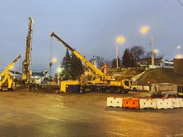 equipo de construcción en el sitio de reparación del paso elevado. una grúa metálica alta y amarilla transporta grandes bloques de hormigón a grandes alturas. maquinaria de construcción detrás de la valla foto