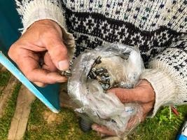 el hombre sostiene un paquete con varias herramientas de reparación. un hombre atraviesa clavos, tuercas, pernos. bolsa de plástico para el almacenamiento de pequeños materiales para la reparación foto