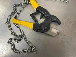 Large iron sharp metal scissors, metal cutters with chains, lie on an iron table. Hand-held locksmith tools. The background photo