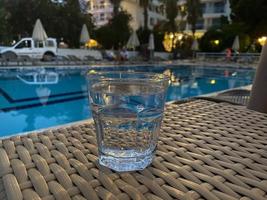 un vaso con una deliciosa bebida alcohólica clara frente a la piscina por la noche de vacaciones en un resort tropical en el hotel foto