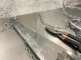 Large iron sharp metal scissors, metal cutters and a saw with chains lie on an iron table. Hand-held locksmith tools. The background photo