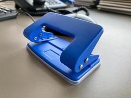 punzón de oficina de metal de hierro azul para perforar agujeros en hojas de papel y documentos en la mesa de trabajo de la oficina. papelería foto
