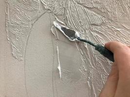 The artist's hand plasters the canvas with a small spatula with acrylic volumetric white paint in the artist's creative arts workshop with paints and brushes on the table of the art school photo