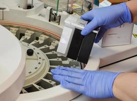 a doctor in gloves performs a cassette with a reagent for performing studies in the analyzer. setting up a calibrator and controls to perform accurate medical tests photo