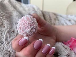 una hermosa mano femenina con uñas rosadas y manicura sostiene un hermoso caramelo rosa delicioso foto