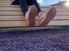 A woman in beautiful sportswear with pink sneakers on her feet sits on a fashionable new bench lounger in the park with purple pebbles for landscape design photo