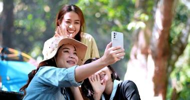 handheld shot, groep jonge vrouwen die kamperen in het natuurpark hebben samen een videogesprek op smartphone met geluk video