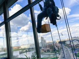 fuera del edificio de varios pisos lavado de la fachada de un escalador industrial ventanas limpias, vista inferior. trabajador alpinista foto