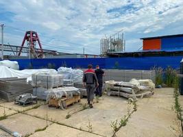 Male workers walk through a warehouse of industrial equipment and materials in boxes in an open-air storage area. View from the back photo