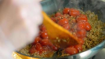 mengen de ingrediënten voor de chorizo en de bewaard gebleven tomaten met een houten lepel. macro het schieten video