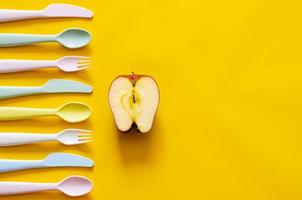 Colorful fork, spoon and knife with cutting apple on yellow background with empty space for text. photo