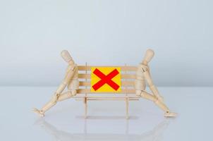 dos modelos de madera sentados en un banco y mantienen la distancia con el espacio para proteger la infección de la gripe. foto