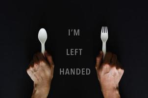 Left handed person holding the spoon on left side with black background for International left handers day concept photo