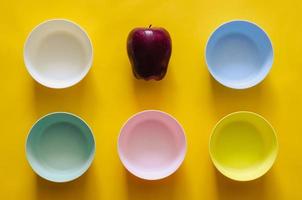 An apple put among the colorful small bowls on yellow background for vegan concept. photo