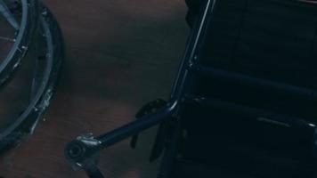 lato Visualizza di uno americano maschio lavoratori nel un' laboratorio a un' fabbrica fabbricazione sedie a rotelle, seduta a un' banco di lavoro utilizzando mano utensili e assemblaggio parti di un' Prodotto, seduta nel sedie a rotelle video