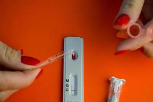 test for coronavirus on an orange background. a sensitive strip, a girl with a bright red manicure drips onto a drop of blood for a test and adds a physical solution there photo