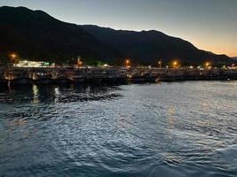 Beautiful coast and beach with outlines of mountains against the backdrop of a sunset from the sea or ocean and burning city lights photo