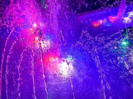 A beautiful night singing fountain with jets of water and splashes with multi-colored illumination. The background photo