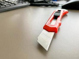 Red sharp office stationery knife with a paper cutting blade on a desktop office desk. Business work