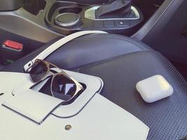 White women's beautiful fashionable leather bag and sunglasses with wireless headphones lie on the leather armchair of a good expensive car photo