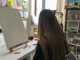 mujer artista con cabello largo dibuja una imagen en el taller de artes creativas del artista con pinturas y pinceles en la mesa de la escuela de arte foto