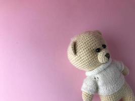 interior toy - a soft knitted bear on a pink background in the corner of the background. bear made of natural materials, crocheted of threads. cute gift photo