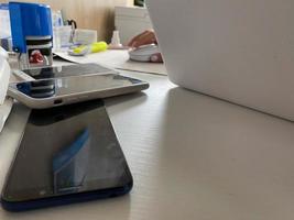 Two working touchscreen mobile phones, smartphones lie on the table in the office with stationery, a stapler, a seal and a laptop photo