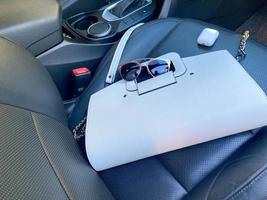 White women's beautiful fashionable leather bag and sunglasses with wireless headphones lie on the leather armchair of a good expensive car photo