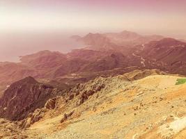 sandy high mountain. high mountain with plants in a warm country. vacation in the mountains. mountain of stones, sand on the surface. against the background next to the mountain blue sea photo