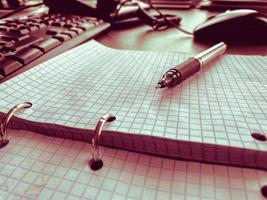 Open notebook with pen lying on it on beige desktop. Notepad sheets on silver brackets, automatic ballpoint pen in silver-black photo