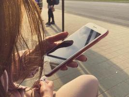 Woman holding a smart phone with empty screen sitting outdoors at the cafe with cake and coffee on the table photo