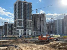 A large construction site of new tall large houses of concrete monolithic-frame buildings with cranes and construction equipment during the repair of new buildings in a large densely populated city photo