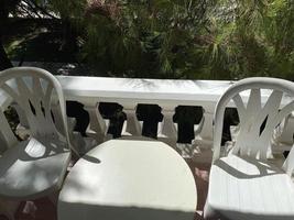 Two white chairs with a table on which stands a breakfast of coffee and croissants on the balcony photo