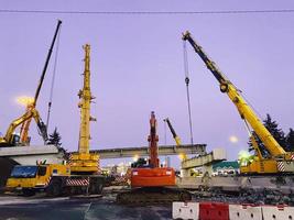 construction of a broken bridge on a busy road. construction equipment on a section of the road erects an overpass behind a plastic barrier photo