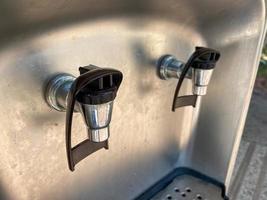 Metal shiny chrome faucets of a cooler with water and drinks, close-up view. Faucet for pouring drinks photo