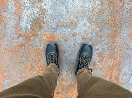 Legs of a man in boots on the background of a rusty old iron red scratched metal corrosed sheet surface background, texture industrial in loft style photo