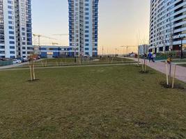 un césped verde con hierba y nuevas plántulas de árboles jóvenes entre las casas altas de nuevos edificios en el patio de una gran ciudad en la megalópolis foto