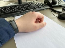 A man's hand in a shirt and with a clock on the table at the office table with a computer with a keyboard. Business work photo