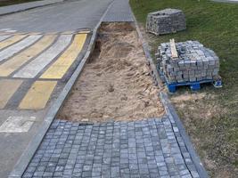 Construction of a sidewalk walkway from concrete paving slabs next to a pedestrian crossing and a speed bump