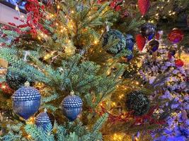 Blured photo of shiny toys and garland hanging on fir branches