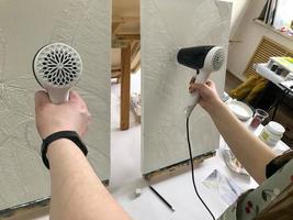 The hands of two artists are drying a plaster with a white voluminous paint on the canvas with a hairdryer. The creative process of art in the school of arts photo