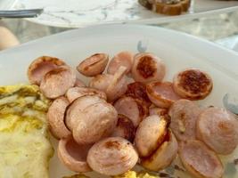 Hearty delicious high-calorie breakfast of fried sausages, sliced sausages on a plate with eggs and omelet photo