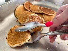 A beautiful hand of a girl takes with tongs delicious flour pancakes for breakfast from a plate in a canteen cafe. The background. Texture photo