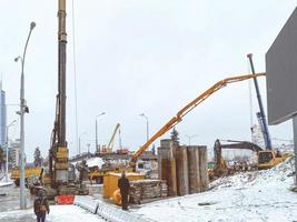 construcción de un puente en el centro de la ciudad en invierno bajo la nieve. máquinas para mezclar hormigón y crear asfalto. construcción de grandes estructuras de hormigón foto