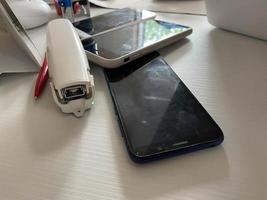 Two working touchscreen mobile phones, smartphones lie on the table in the office with stationery, a stapler, a seal and a laptop photo